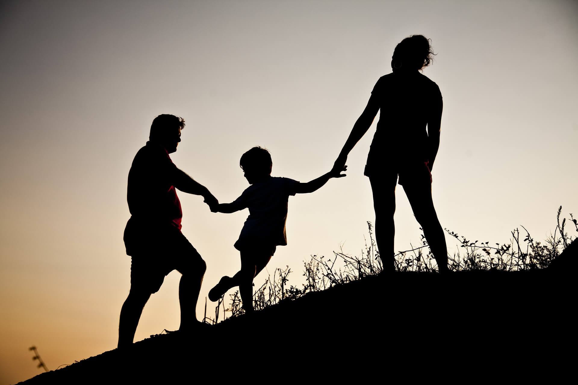 Familieopstellingen. Silouet van Ouders en jong kind hand in hand de helling op.